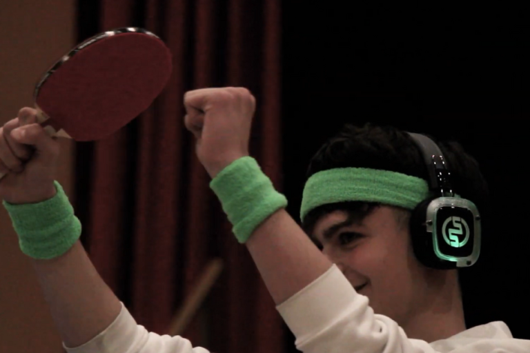 Ragazzo con dei polsini verdi e delle cuffie alle orecchie che regge una racchetta da ping pong